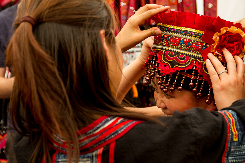 A traditional Hmong clothing vendor helps Melodie Vang to put on a traditional hat.